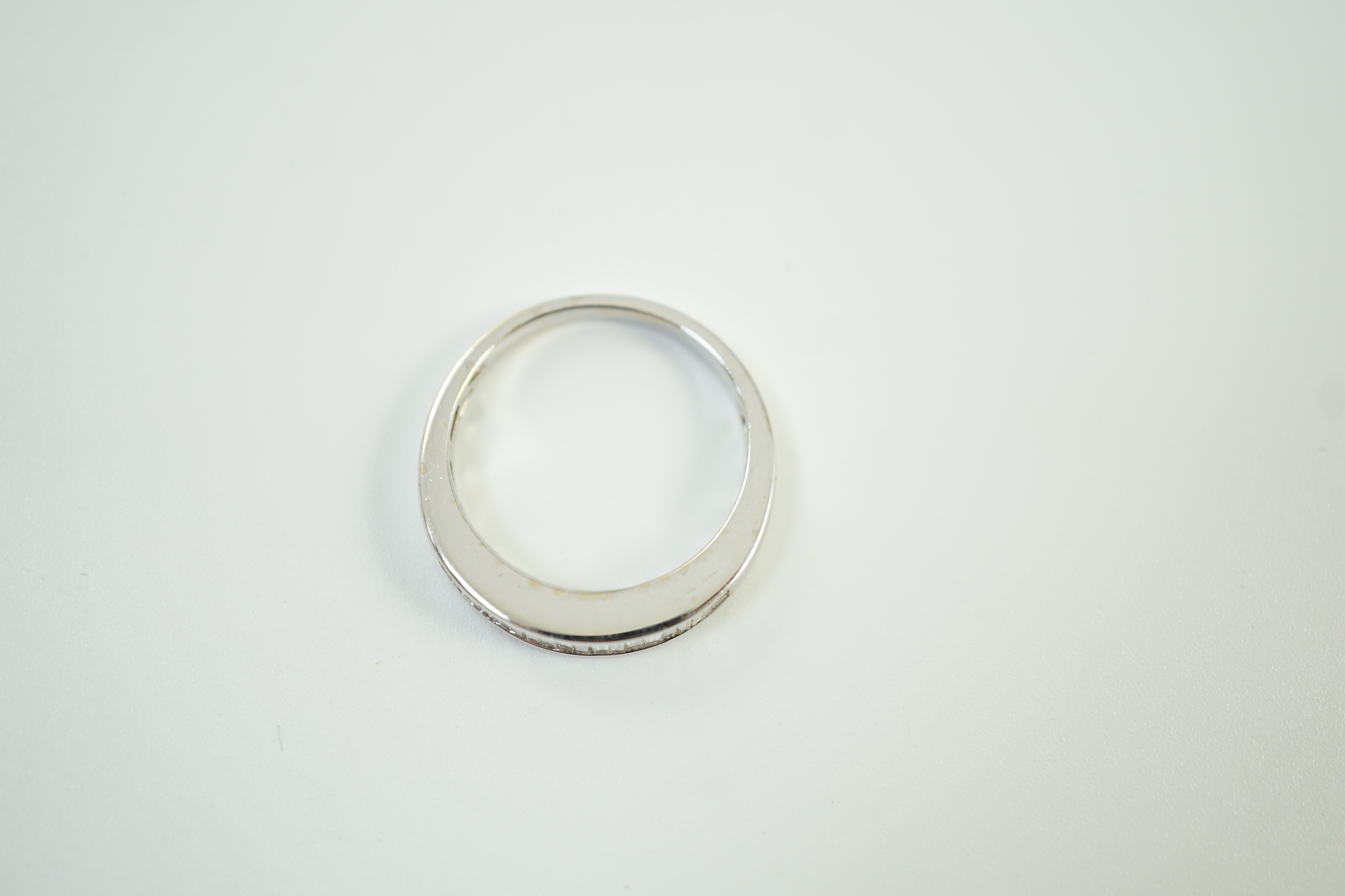 A modern white metal and graduated baguette cut channel set diamond half hoop ring, size M/N gross weight 3.7 grams.